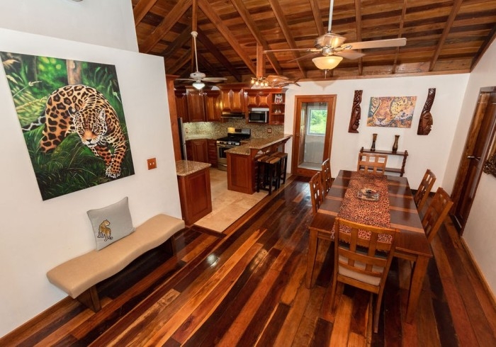 View from loft into dining area, beautifully stained wood floors and ceilings, dining set with picture of jaguar on wall and partial view of kitchen to the left