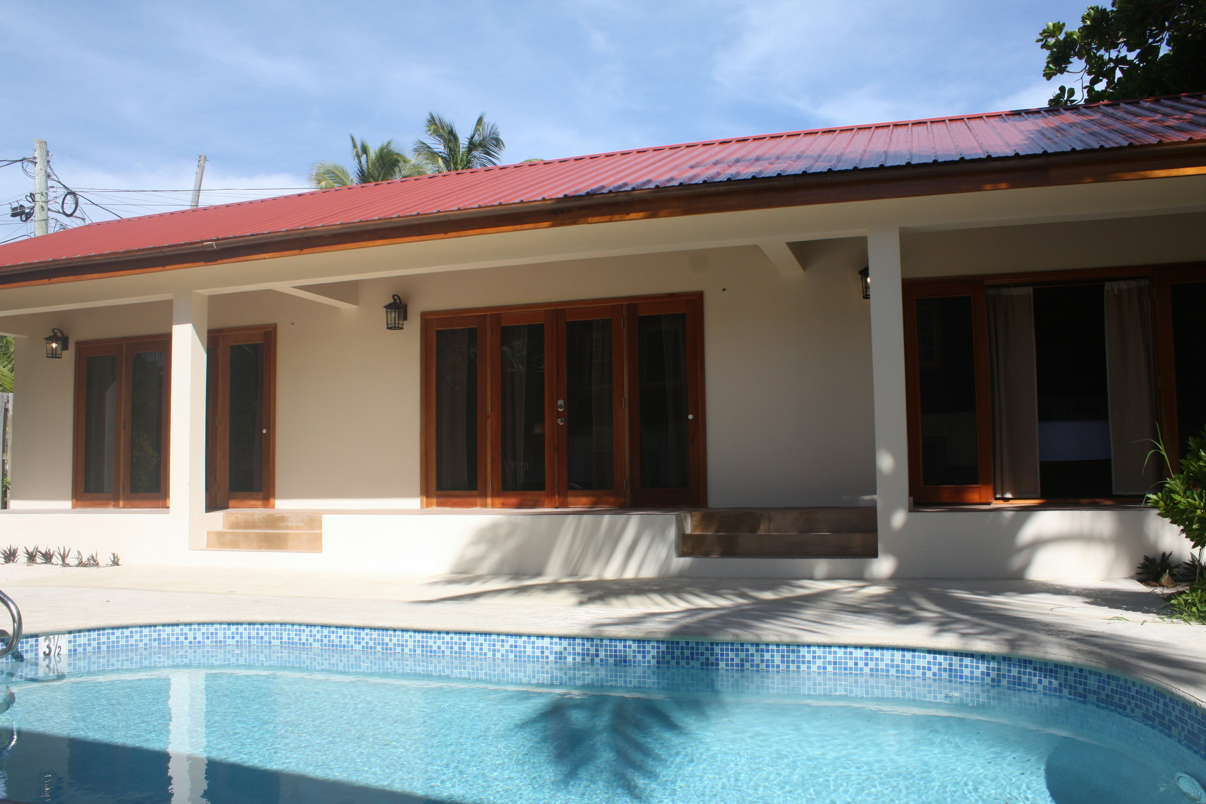 Pool deck in foreground with steps up to exterior of long white building with red roof and three sets of french doors