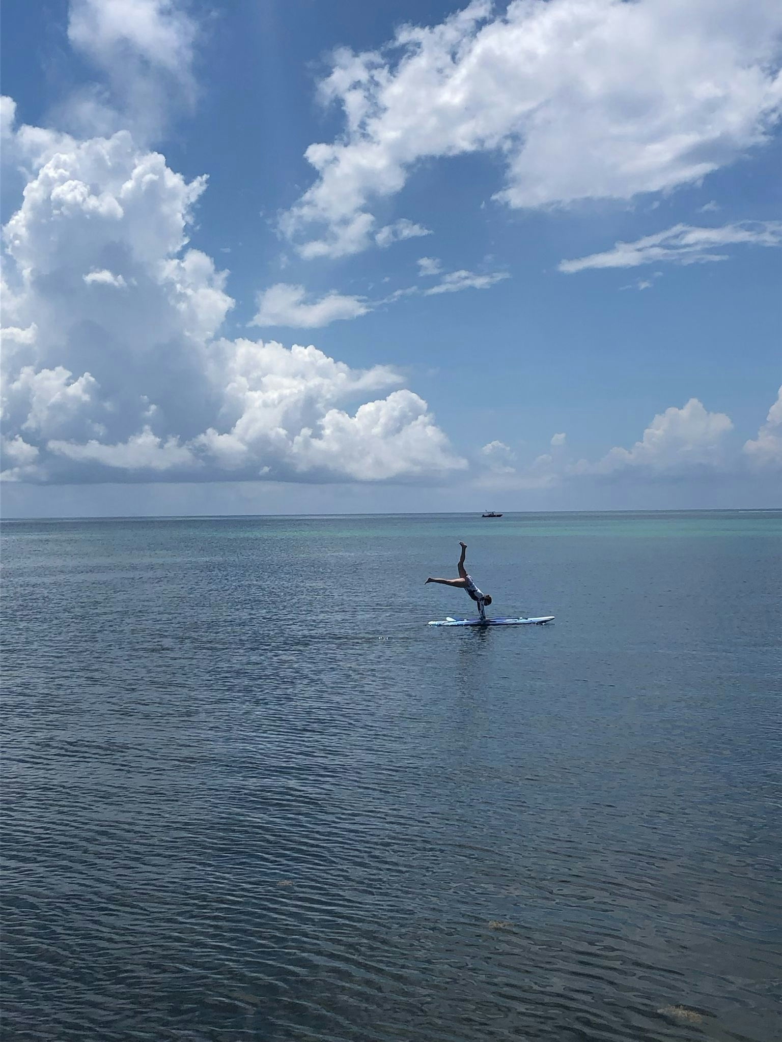 A person doing a handstand on a paddleboard on the ocean with blue skies above