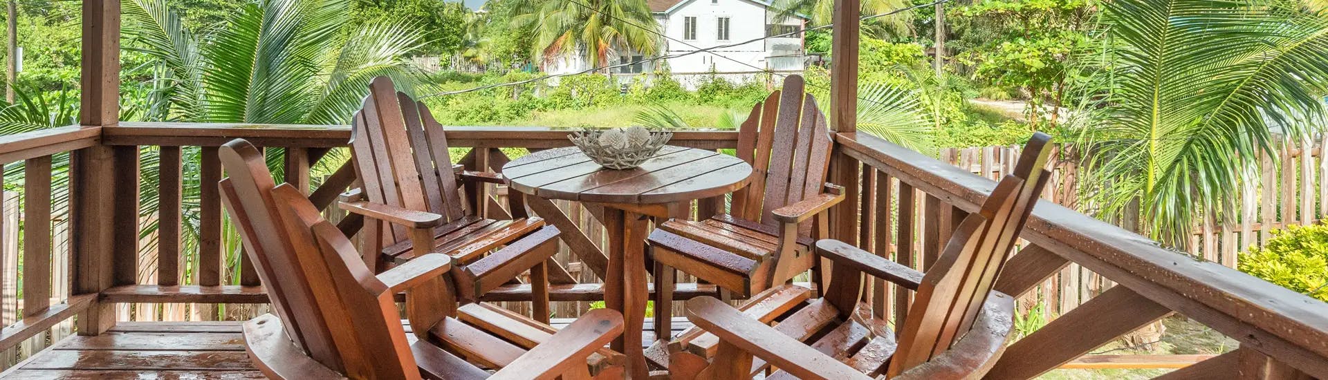 Wooden balcony with round wooden table and decorative basket centerpiece and four matching chairs overlooking greenery and palms