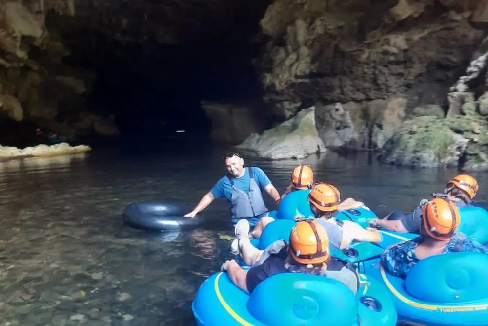 Group of people sitting on individual blue inner tubes on water heading into rocky cave entrance