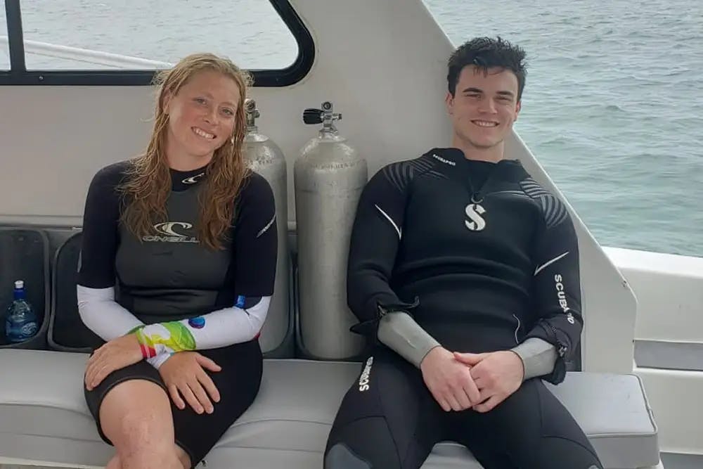 Smiling young woman and young man in scuba gear sitting on boat in front of scuba tanks