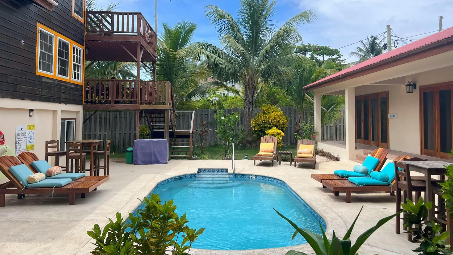 wood three story building, exterior wood stairs, oval pool and wood deck chairs with view of king room french door access on the other side of the pool