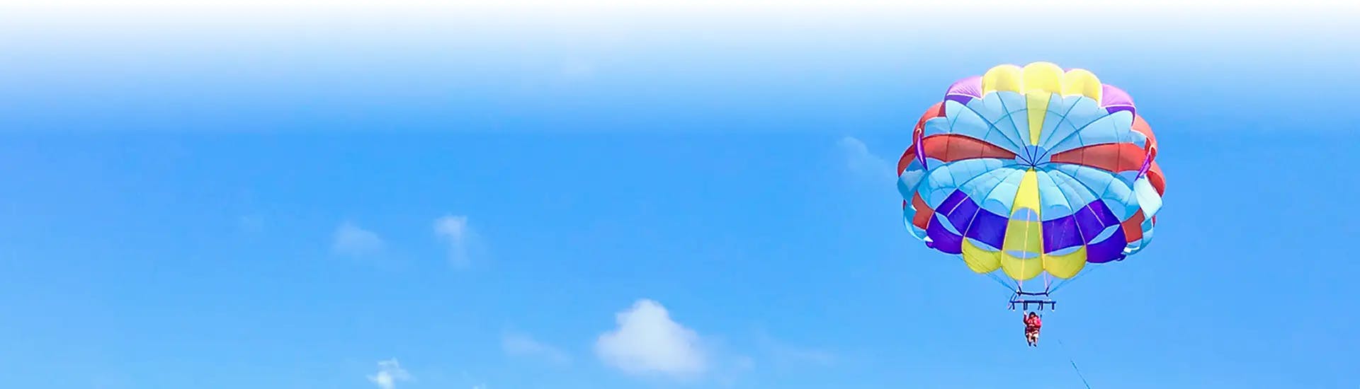 Multi-color parasail over blue ocean and under blue and white cloudy sky