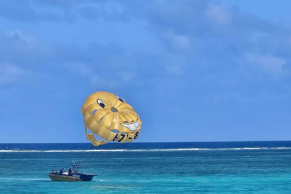 Boat towing a yellow parasail on blue ocean waters with blue sky and wispy clouds above