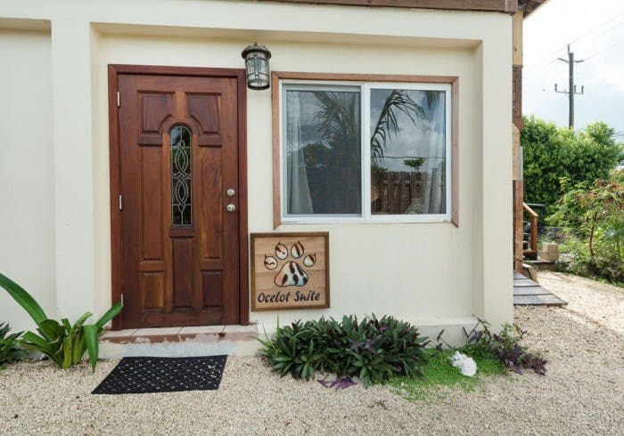 Exterior dark wooden door with decorative light above, windows, sign with animal paw print with the words "Ocelot Suite"