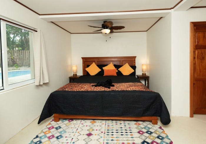 Wooden bed with black sheets and animal print cover, throw pillows, nightstands with matching lamps, and ceiling fan