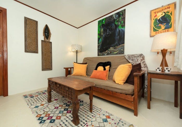 Wood living room set with sofa, end tables, lamps and coffee table, large picture of black panther behind sofa, and picture with toucan and words "Toucan Belize"