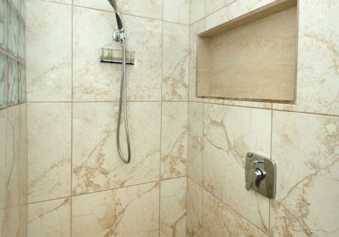 Interior of tiled shower in neutral shades with silver fixtures and flexible hand-held shower head