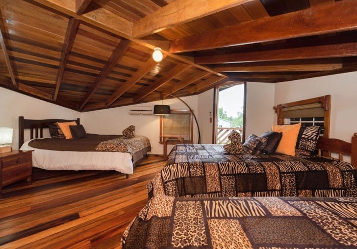 Loft area with richly stained wood ceilings and floors, three beds adorned with animal print bedding, nightstands with lamps, and exterior door leading to balcony