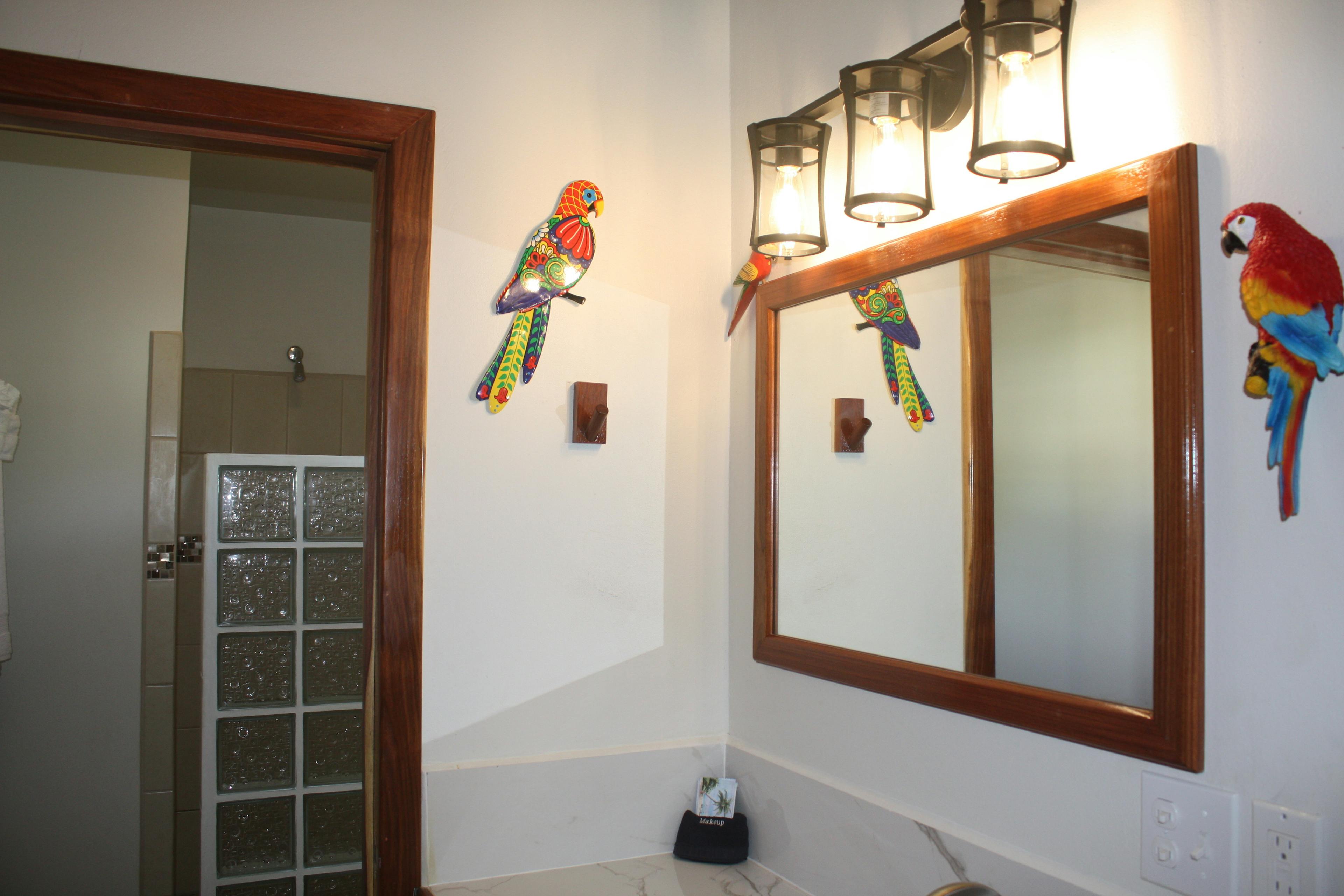 Bathroom mirror over vanity, decorative parrots hanging on walls, and door leading to shower area