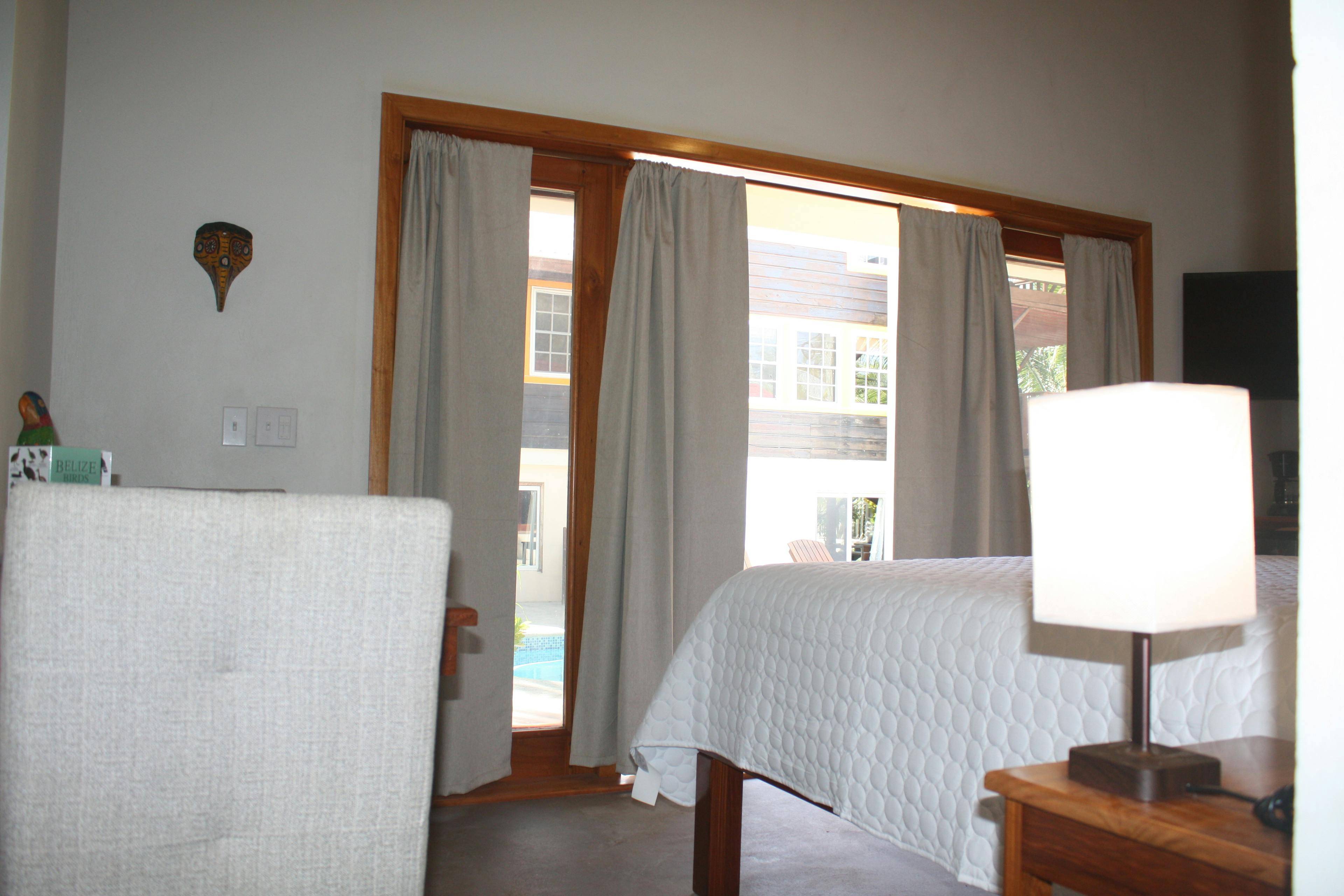 Bedroom looking towards draped french doors with view of pool deck, pool, and building on opposite side