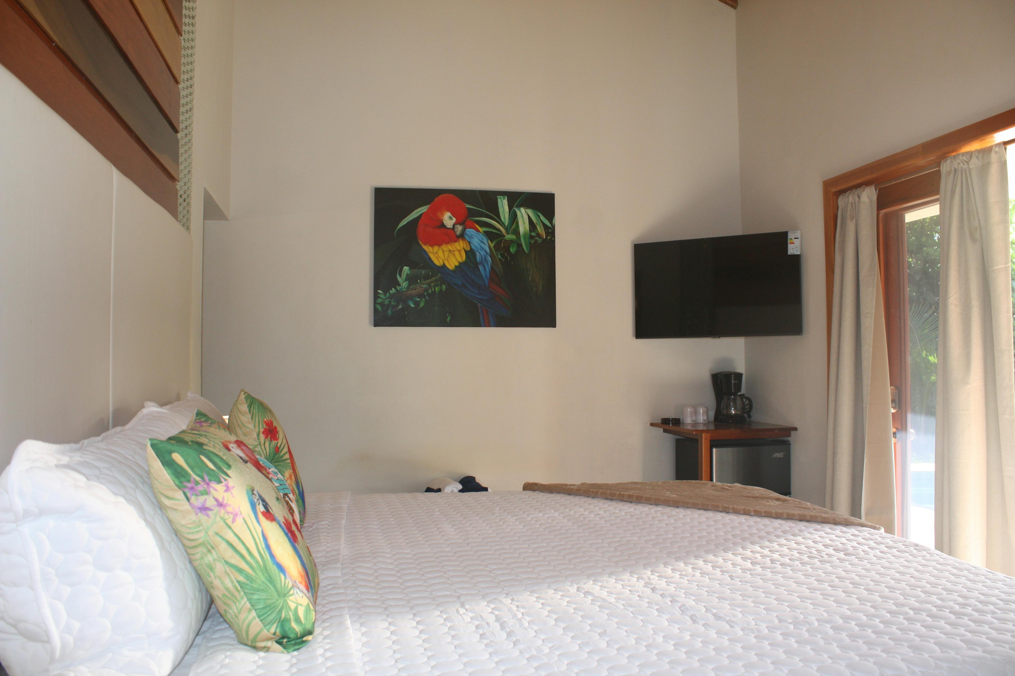 bed with white cover, french doors with dark wood trim, photo of macaw on wall and tv on wall