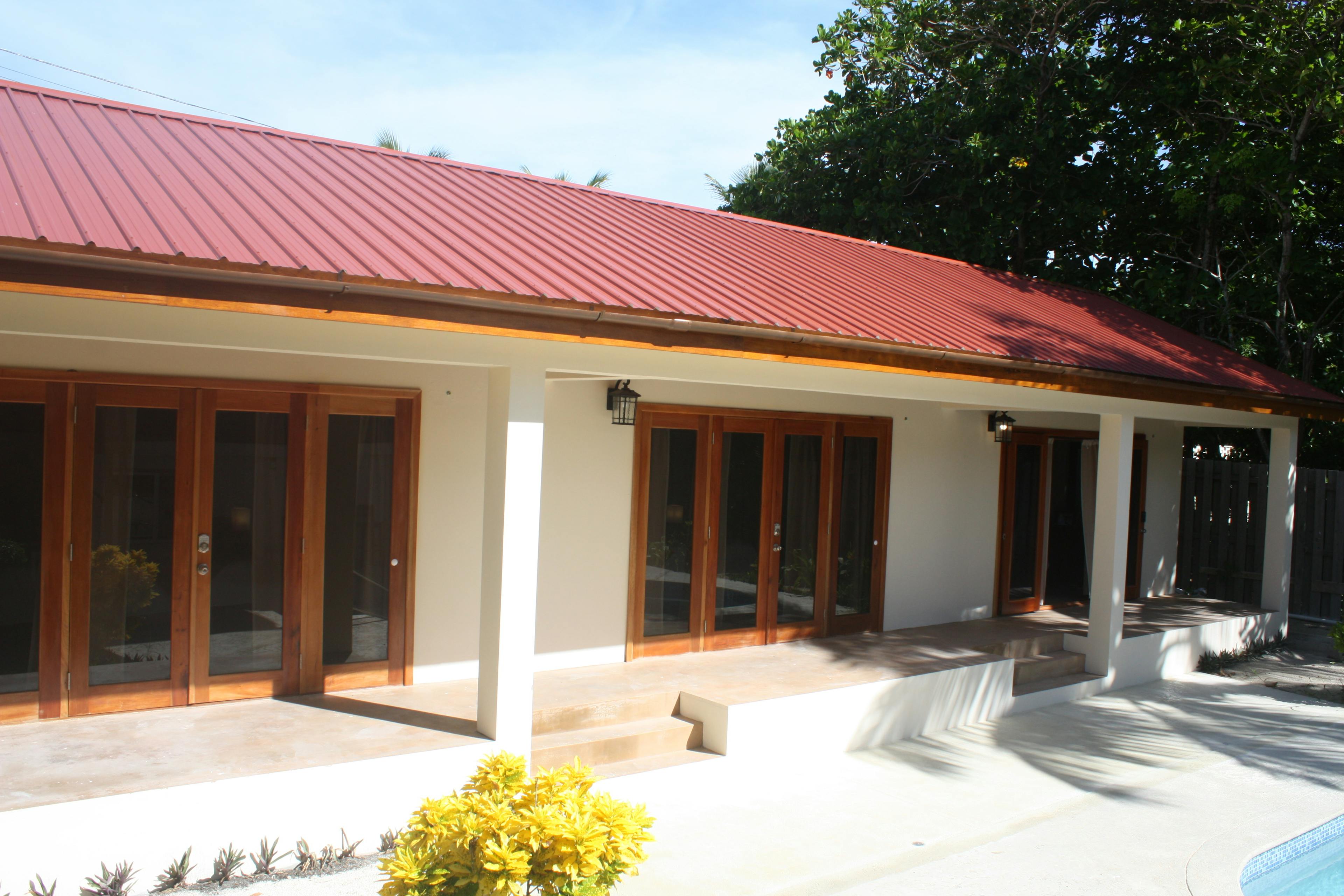 Exterior of long white building with red roof and three sets of french doors with steps leading to pool deck